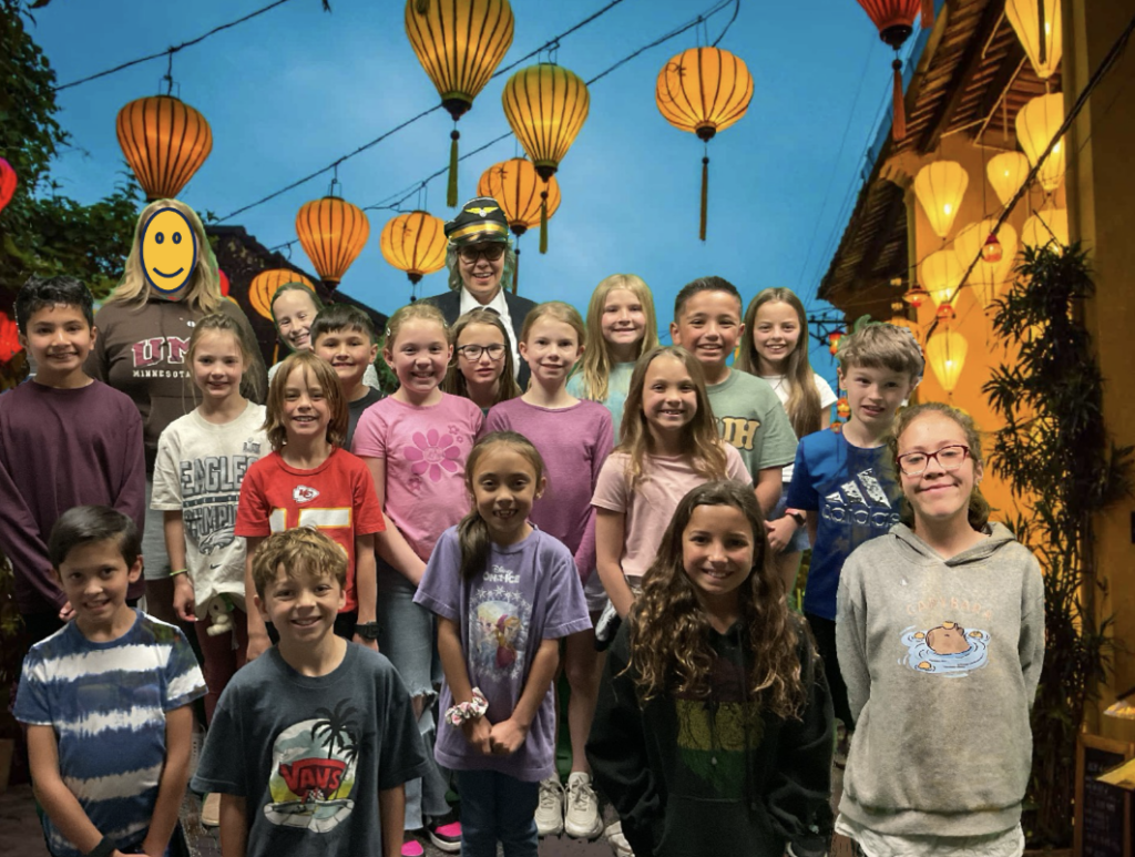 Group photo of children in casual clothing, smiling in front of colorful lanterns against a festive background.